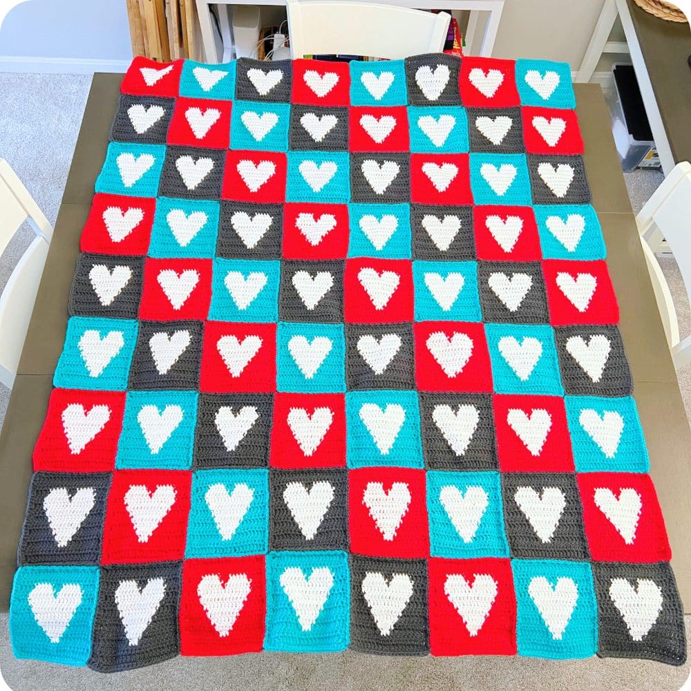Finished crochet heart blanket pattern made from sewn heart squares in red, teal, and gray, displayed flat to show the full repeating heart design.