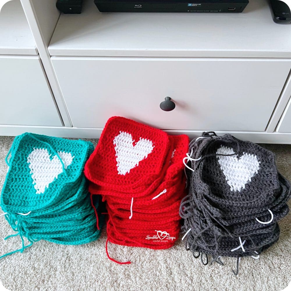 Stacks of completed crochet heart squares in red, teal, and gray yarn, ready to be sewn together for a crochet heart blanket.