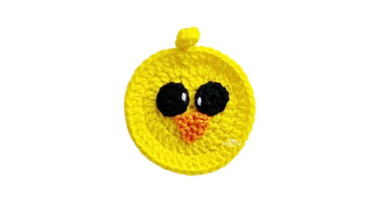 Free crochet chick applique pattern made with bright yellow yarn, featuring a round chick face with black eyes and an orange beak, perfect for beginner crochet projects.