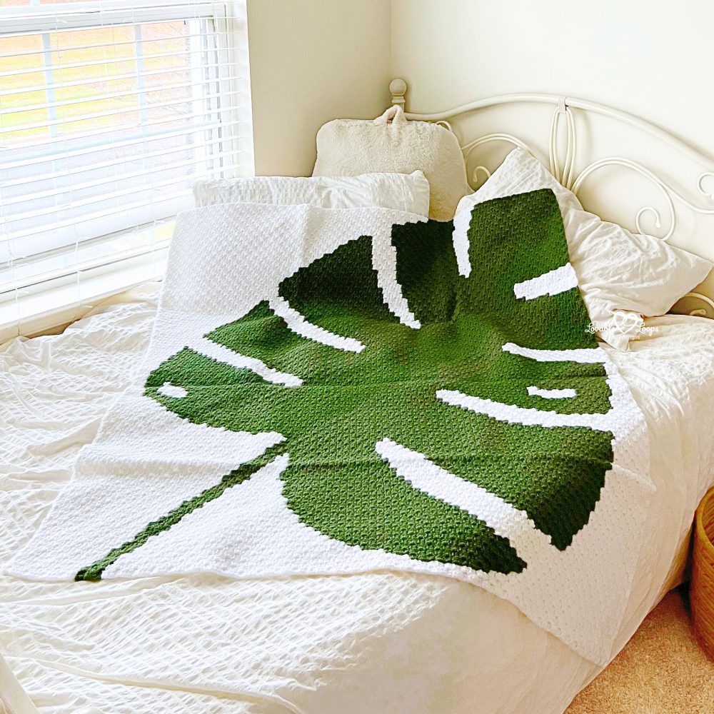 Close-up of a corner-to-corner crochet monstera leaf blanket highlighting the green leaf motif and textured stitches