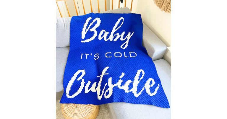 Baby it’s cold outside crochet blanket pattern featuring bold white lettering on a blue corner-to-corner crochet blanket displayed on a couch