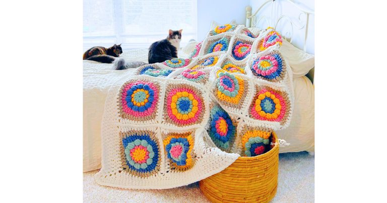 Crochet flower granny square blanket pattern featuring colorful layered flower granny squares with a white border, styled on a bed