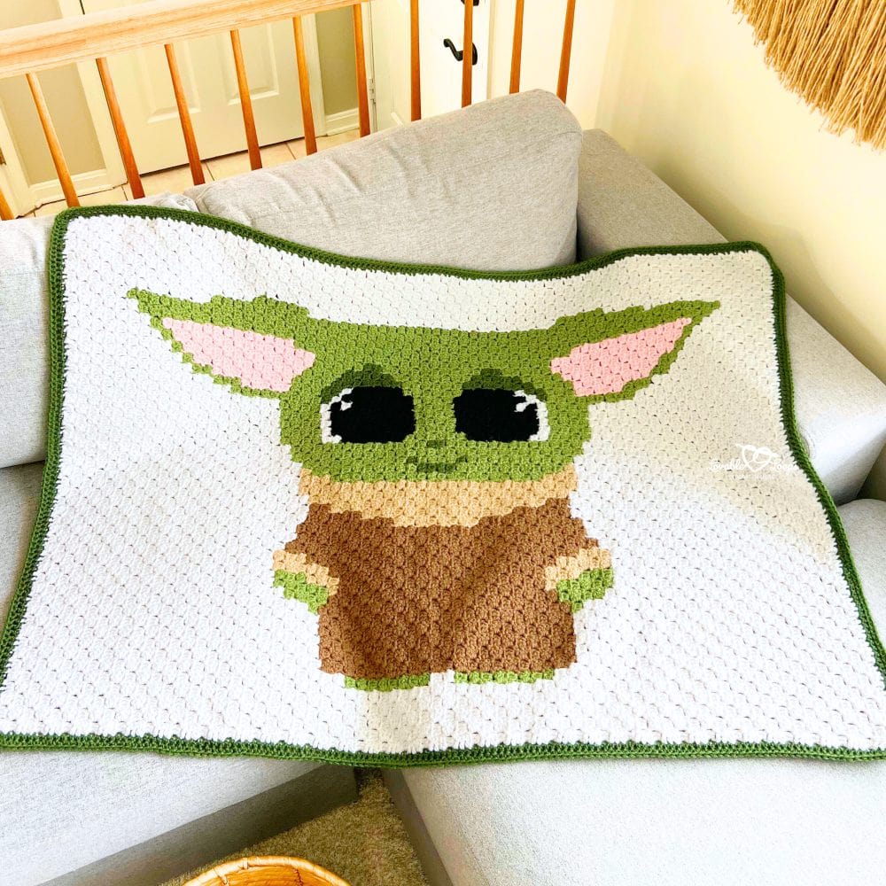 Corner-to-corner Baby Yoda crochet baby blanket with green border, shown draped on a couch