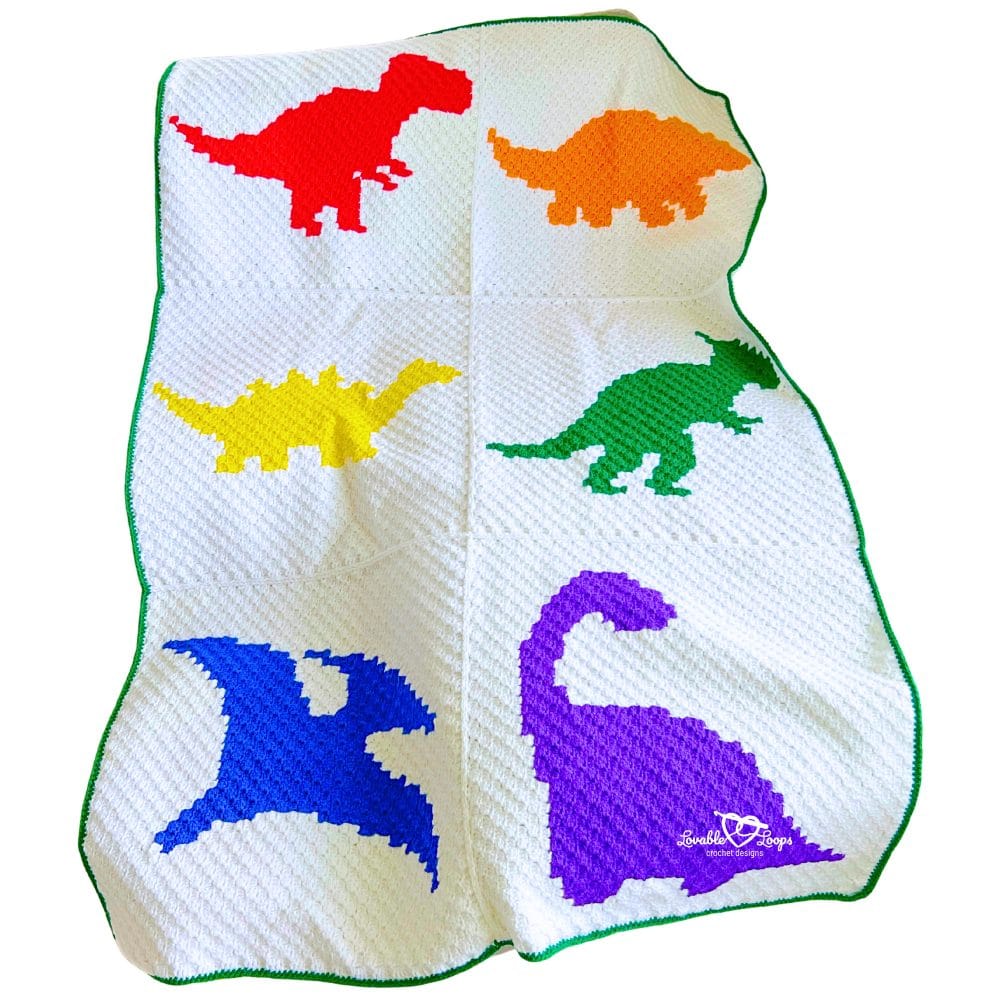 Close-up of a C2C crochet dinosaur blanket showing textured corner-to-corner stitches and six bright dinosaur shapes in red, orange, yellow, green, blue, and purple on a white blanket with green edging.