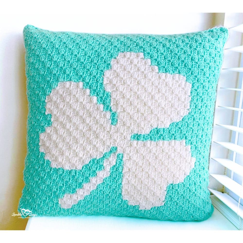 Finished C2C crochet shamrock pillow cover in mint green and white, measuring 19 inches, styled near a window for St. Patrick&rsquo;s Day decor.
