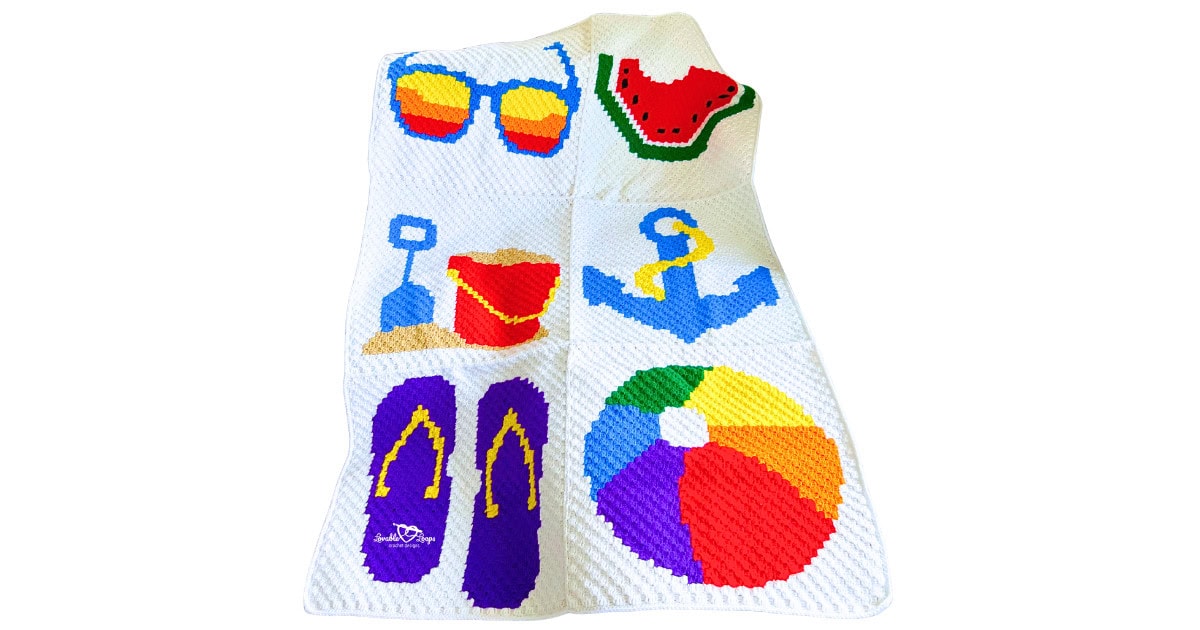 Full view of a C2C crochet blanket made from six joined panels with bright summer motifs, including sunglasses, watermelon, beach toys, anchor, flip flops, and a rainbow beach ball.