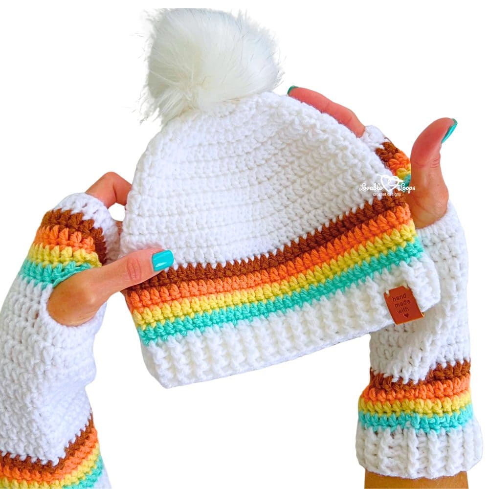 Close-up of a crochet beanie with pom pom showing colorful retro stripes, textured stitches, and a stretchy ribbed brim