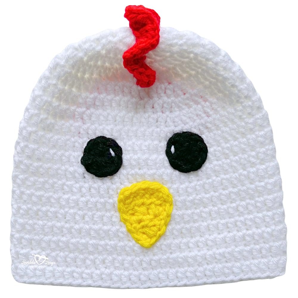 White handmade crochet chicken beanie with a red comb, yellow beak, and simple cartoon-style face.