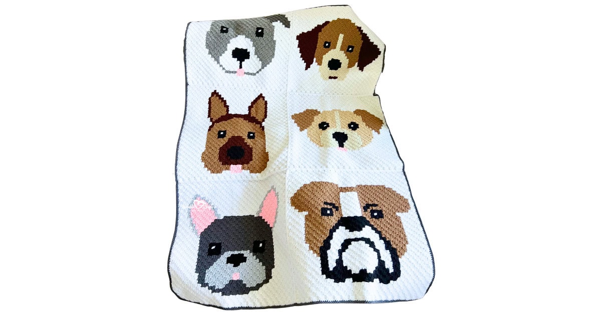 Full view of a corner-to-corner crochet dog blanket with six dog faces arranged in a 2&times;3 layout on a light background with a dark border.