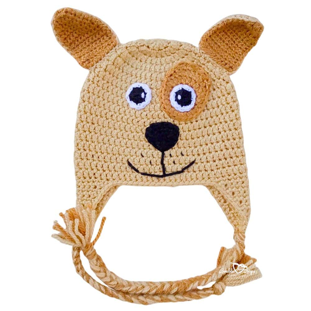 Finished crochet dog hat pattern with earflaps, braided ties, and a cute dog face on a white background.