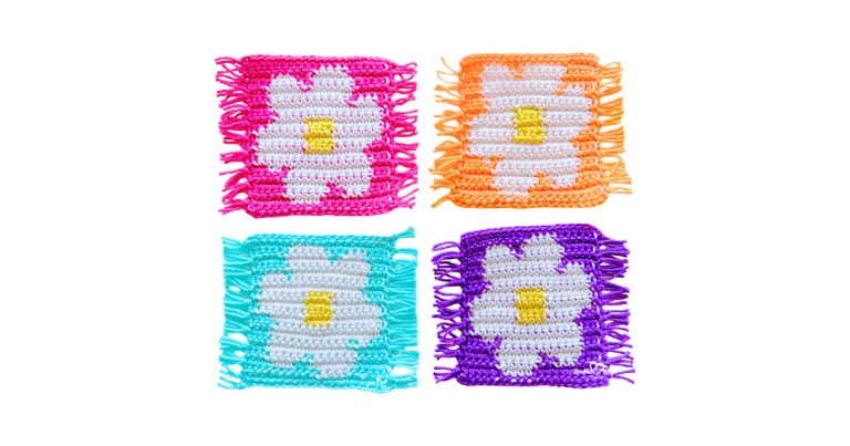 Four crochet flower coasters made with tapestry crochet, each featuring a white daisy with a yellow center on pink, orange, teal, and purple backgrounds with fringe