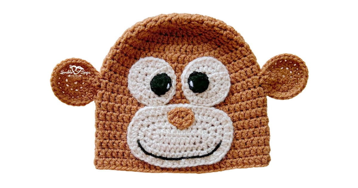 Brown crochet monkey hat with round ears, large eyes, and a cream face applique with a smile.