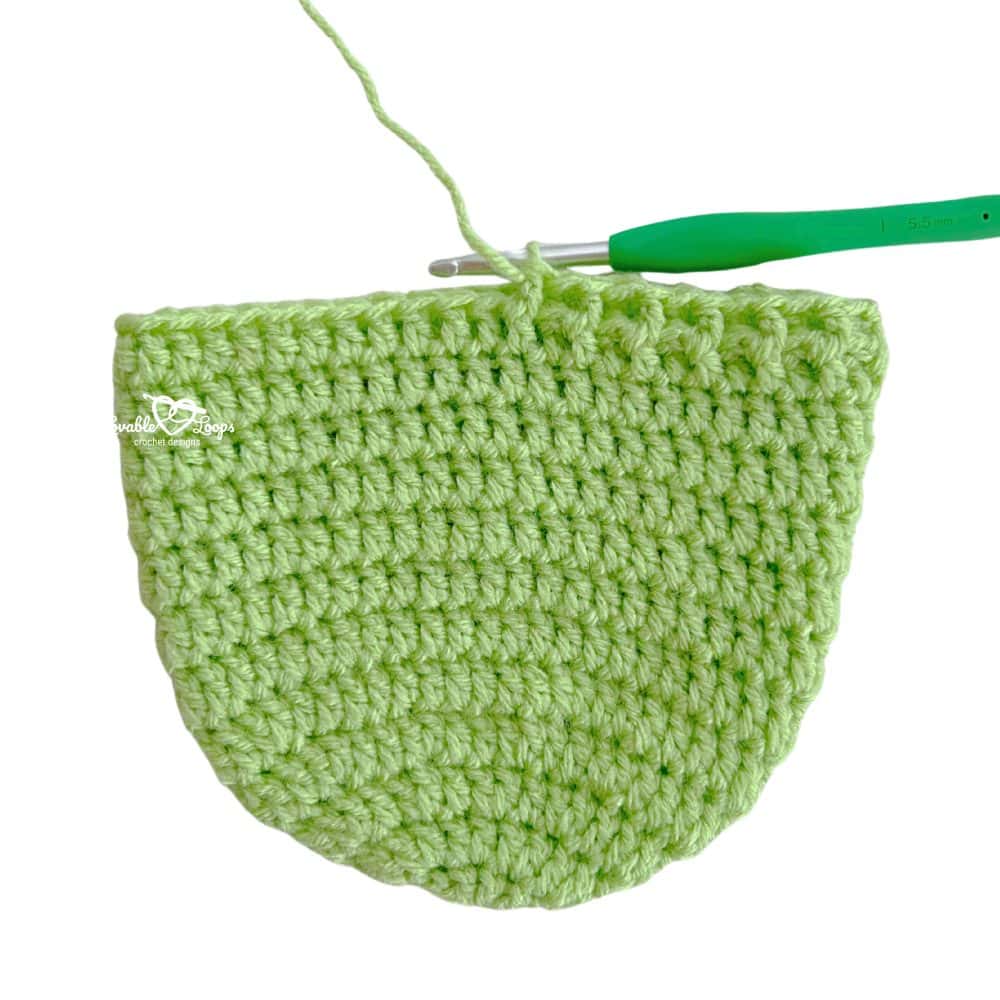 Green crochet newborn hat in progress with a 5.5 mm crochet hook still attached. Easy step-by-step crochet newborn hat pattern for beginners.