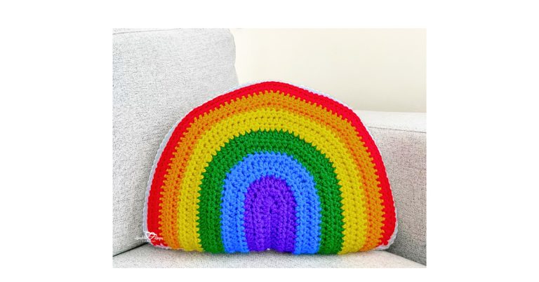 Finished crochet rainbow pillow pattern with purple, blue, green, yellow, orange, and red stripes bordered in white, shown on a couch.