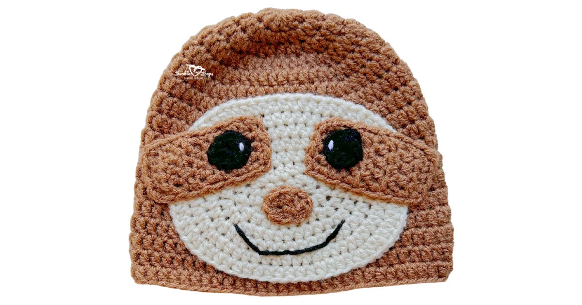 Brown crochet sloth hat with tan face and eye mask details, black eyes, and a stitched smile.