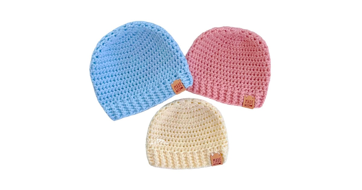 Three crochet baby hats made with the same simple pattern in pastel blue, pink, and cream yarn. Each beanie features a ribbed brim and smooth crown, laid flat. These hats are made using beginner-friendly stitches and follow the free easy crochet baby hat pattern.