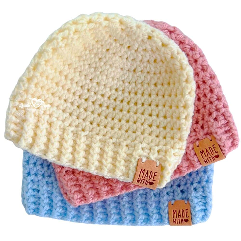 Close-up of three stacked crochet baby hats in ivory, blush pink, and baby blue. These soft handmade hats have a ribbed brim and are made using a simple and easy crochet pattern for babies.