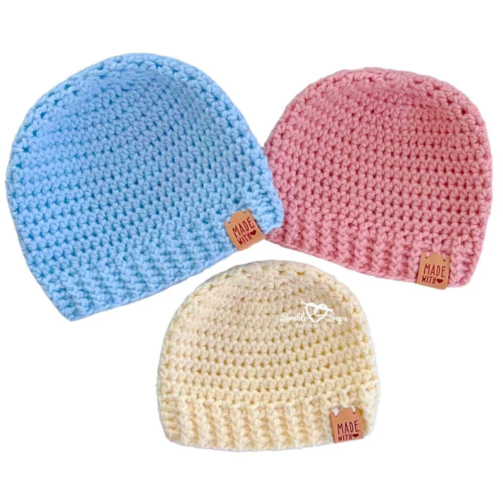 Three handmade crochet baby hats in blue, pink, and cream yarn displayed in a flat lay. These beginner-friendly baby beanies use basic stitches and are part of a free crochet baby hat pattern.