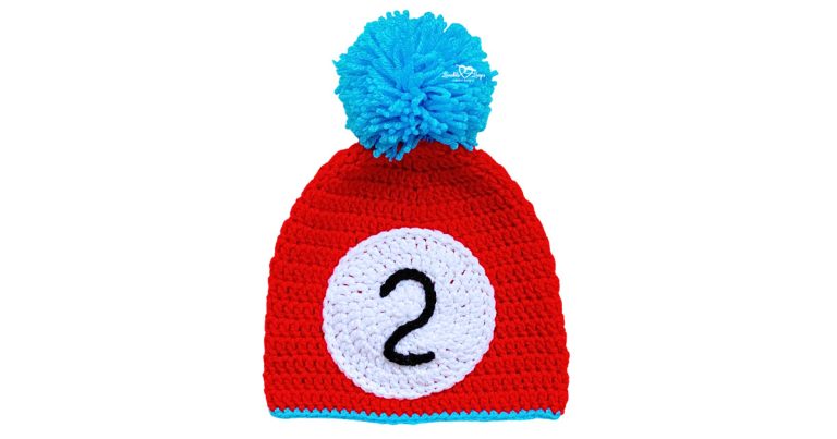 Red Read Across America crochet hat with white circle appliqu&eacute;, black number 2, and bright blue pom pom.