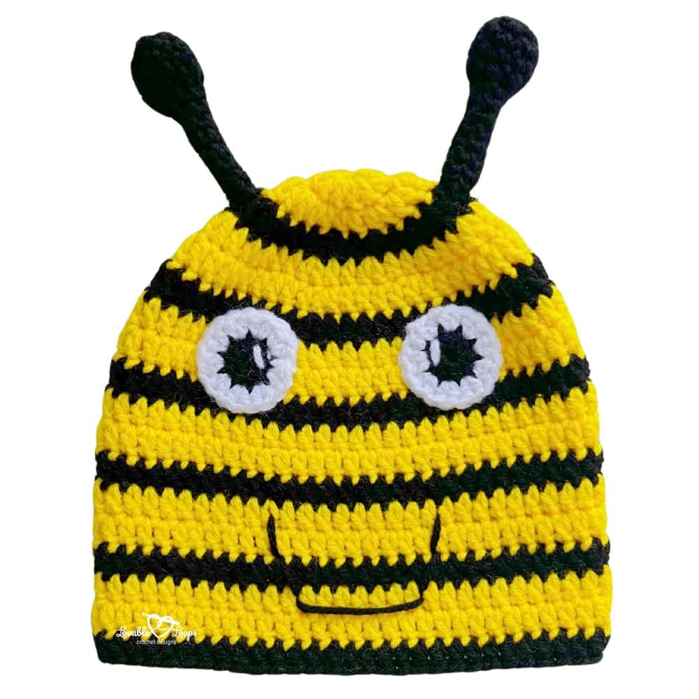 Handmade crochet bee beanie in bright yellow and black stripes with big eyes, a smiling face, and soft antennae.