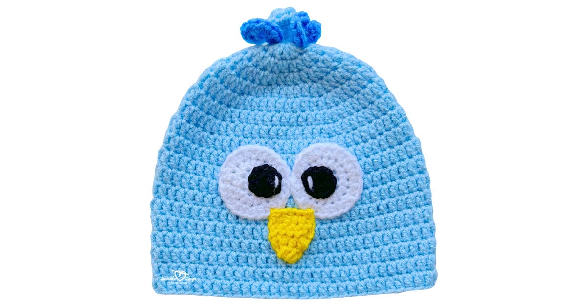 Light blue crochet bird hat with large white and black eyes, a yellow beak, and a small blue tuft on top.