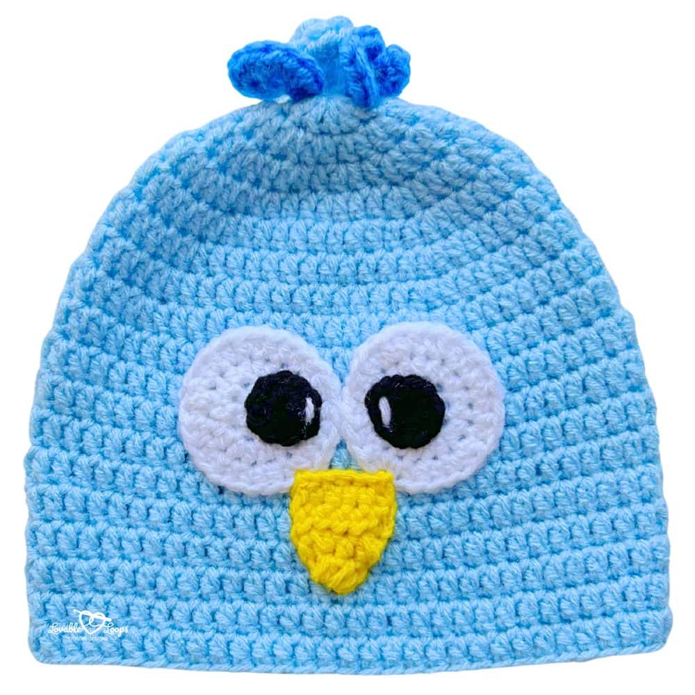 Blue crochet bird beanie with oversized eyes, a yellow beak, and a playful feather tuft at the top.