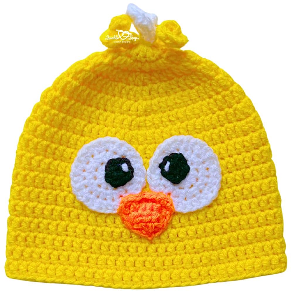 Yellow crochet chick beanie with oversized eyes, an orange beak, and a curly tuft detail on top.