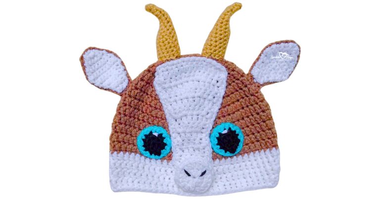Front view of a crochet goat hat with brown and white color blocking, floppy ears, yellow horns, and blue eyes on a white background.