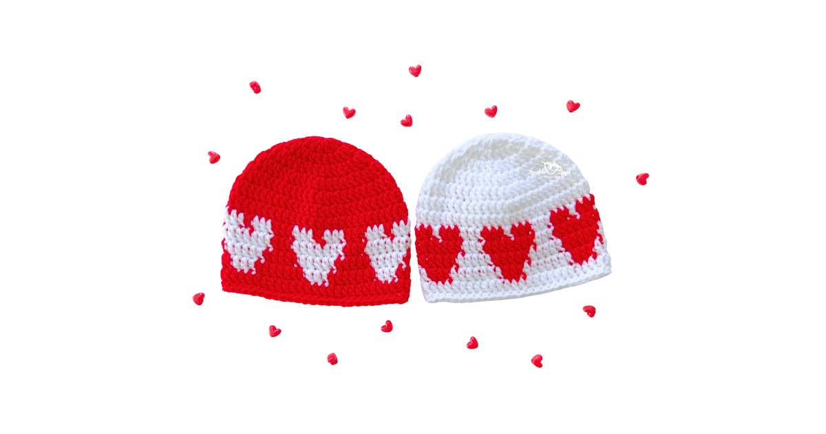 Two baby beanies made from a crochet heart hat pattern: one red hat with white hearts and one white hat with red hearts; beginner-friendly crochet baby hat pattern sized 6&ndash;12 months.