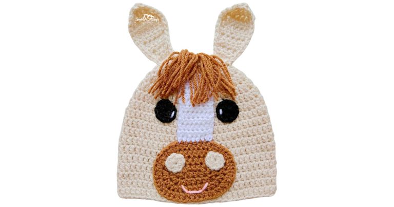 Cream crochet horse hat with upright ears, brown yarn mane, white face stripe, and a brown muzzle with a smile.