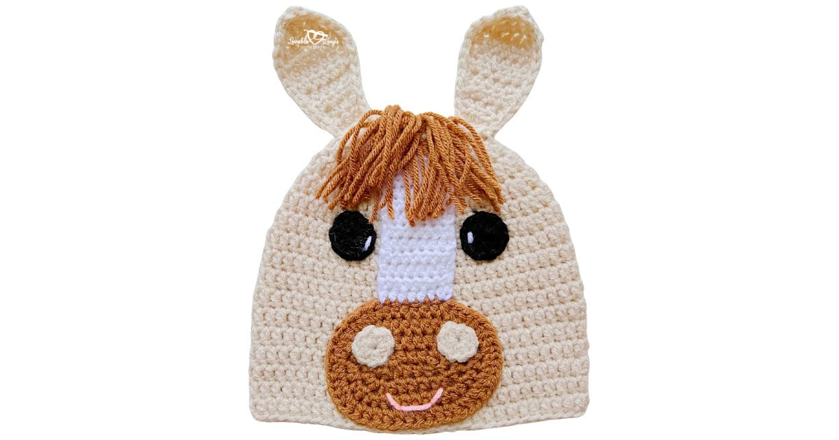 Cream crochet horse hat with upright ears, brown yarn mane, white face stripe, and a brown muzzle with a smile.