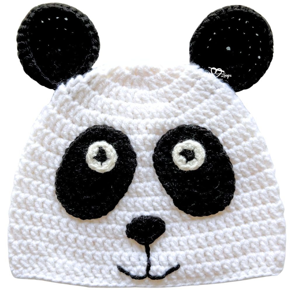 Close-up of a handmade white crochet panda hat with black ears, black eye patches, and embroidered facial details on a light background.