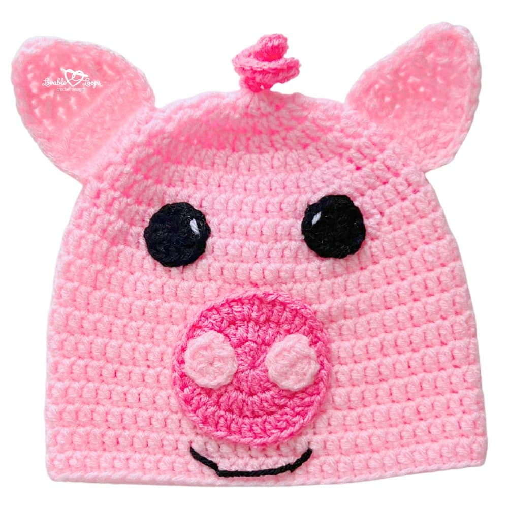 Bright pink crochet pig beanie with little ears, a raised snout, and a sweet smiling pig face.
