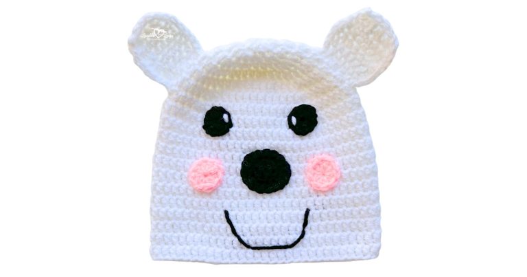 White crochet polar bear hat with round ears, black nose, pink cheeks, and a smiling face.