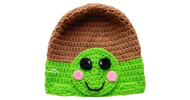 Green and brown crochet turtle hat with a turtle face applique, pink cheeks, and a smiling expression.