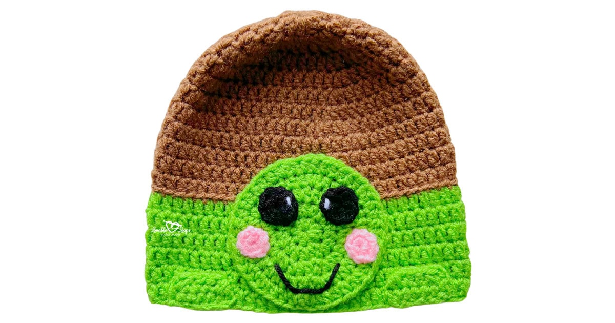 Green and brown crochet turtle hat with a turtle face applique, pink cheeks, and a smiling expression.