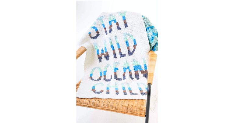 Finished C2C crochet word blanket draped over a chair, featuring an ocean-inspired phrase blanket design in soft coastal colors