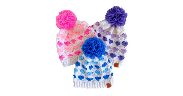 Cute crochet heart beanie pattern in three different colors with rounds of small hearts, a ribbed brim, and a pom pom on top.
