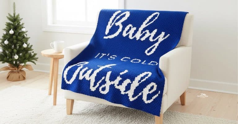 C2C “Baby it’s cold outside” crochet blanket in blue and white draped over a cream armchair in a bright living room with subtle Christmas decor.