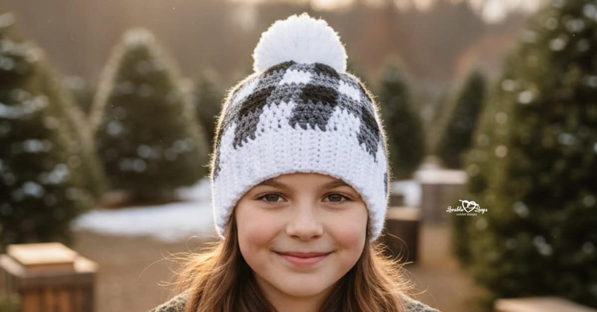 Girl wearing a black, gray, and white buffalo plaid crochet hat with a white pom-pom at a Christmas tree farm