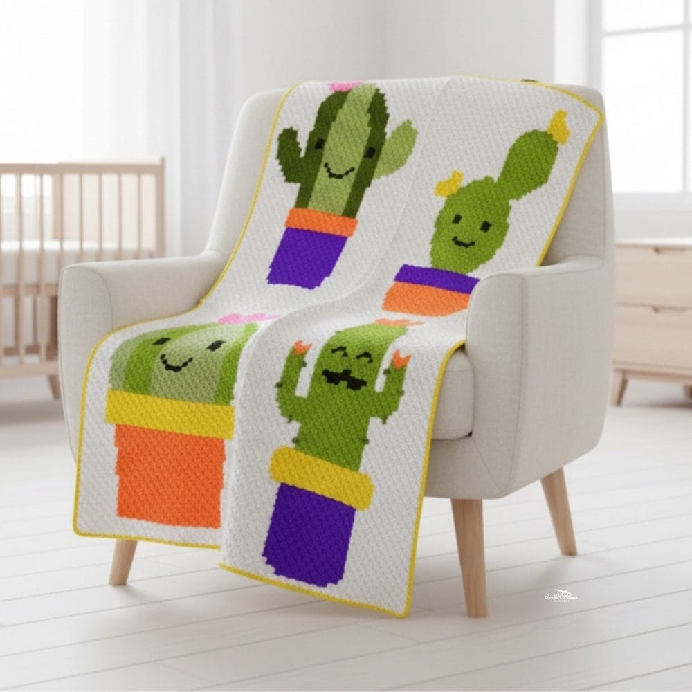 C2C cactus crochet blanket draped over a cream armchair in a bright nursery, featuring four smiling potted cactus blocks in green, orange, purple, and yellow.