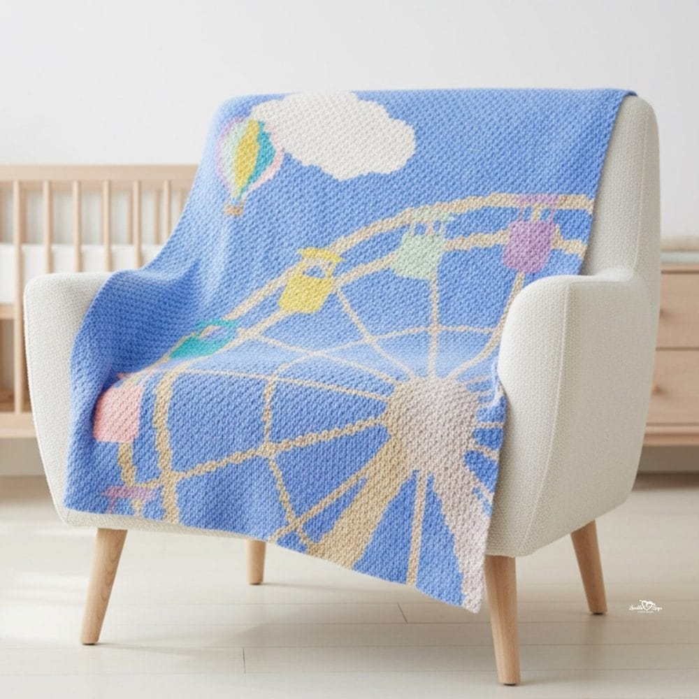 Blue C2C carnival blanket draped over a cream armchair in a bright nursery, featuring a ferris wheel, hot air balloon, cloud, and pastel carnival details.