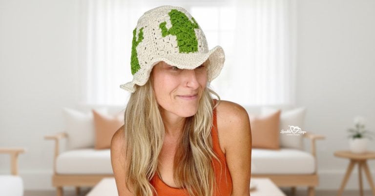 Woman wearing a cream crochet cactus bucket hat and orange tank top, photographed in a bright neutral living room with soft natural light.