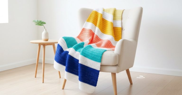 Color block crochet blanket with coral, yellow, teal, navy, and white stripes draped over a cream armchair in a bright room.