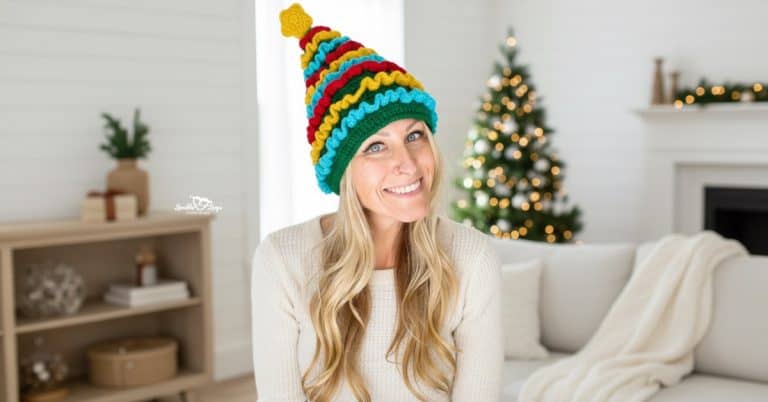 Woman wearing a colorful crochet Christmas tree hat and cream sweater in a bright cozy living room with white furniture and soft Christmas decor