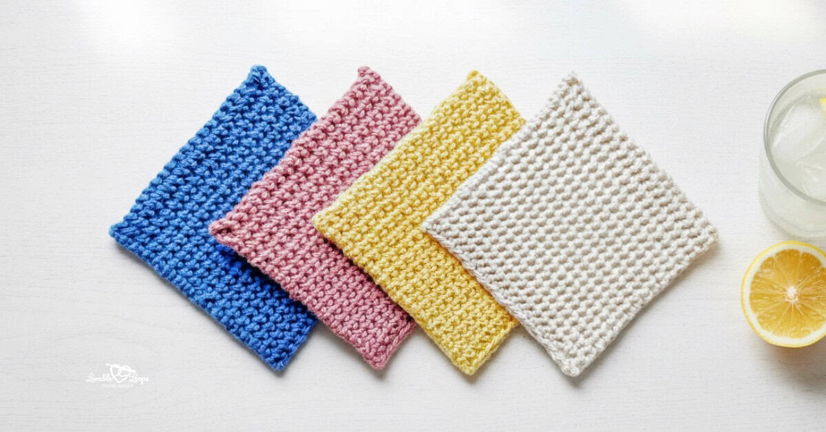 Top-down photo of four beginner crochet coasters in blue, pink, yellow, and cream arranged in a row on a whitewashed table beside a glass of lemonade and a lemon slice.