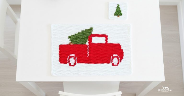 Overhead view of a white crochet placemat on a white table, featuring a red vintage pickup truck carrying a green Christmas tree, with a matching square crochet coaster above it.