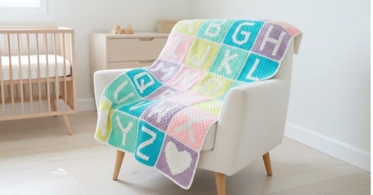 C2C crochet alphabet baby blanket with pastel letter blocks draped over a cream armchair in a bright nursery.