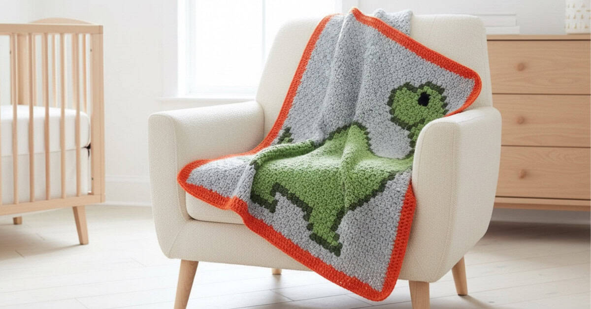 C2C crochet brontosaurus blanket with a green dinosaur on a gray background and orange border draped over a cream armchair in a bright nursery.