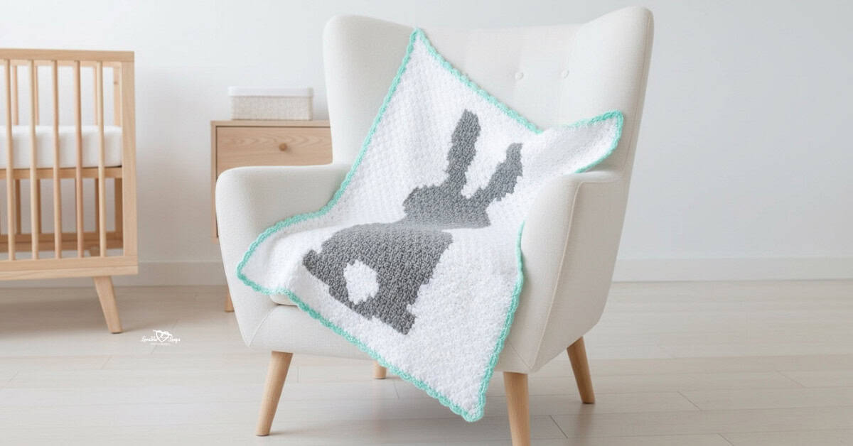 C2C crochet bunny blanket with a gray bunny silhouette and mint border draped over a cream armchair in a bright nursery.